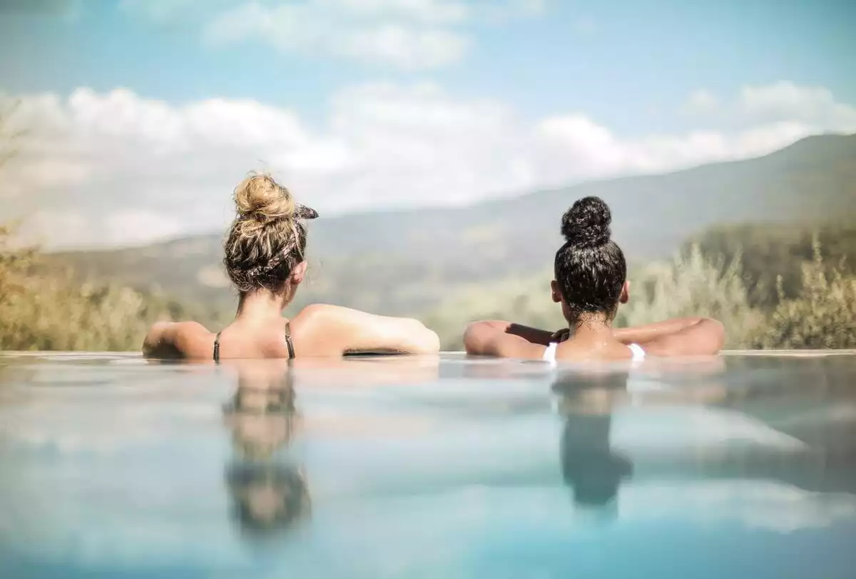 Dos chicas de espaldas metidas en una piscina mirando al horizonte