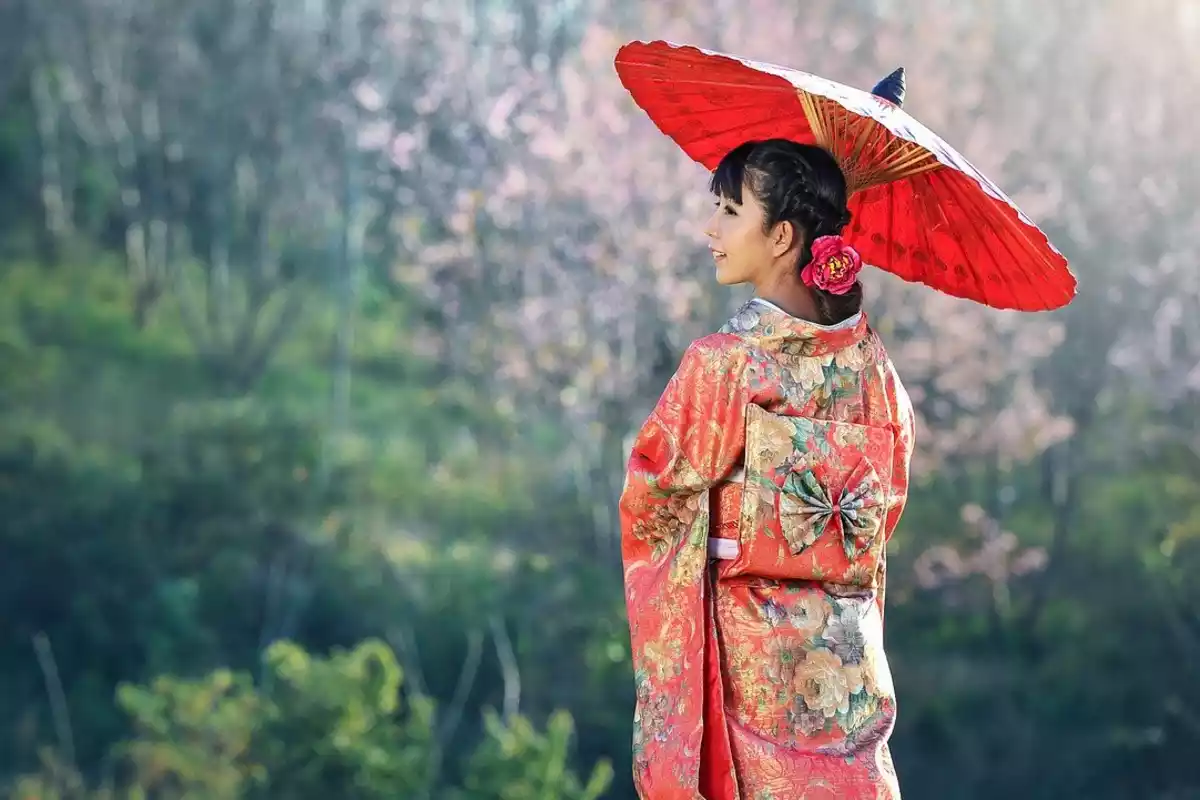 Una mujer japonesa con un tradicional kimono y un paraguas en medio de un paraje natural