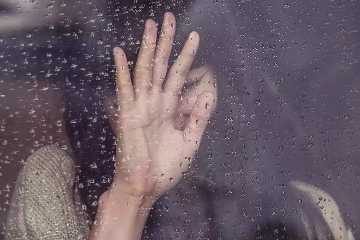 Una mujer triste delante de una ventana, llorando en un día gris de lluvia