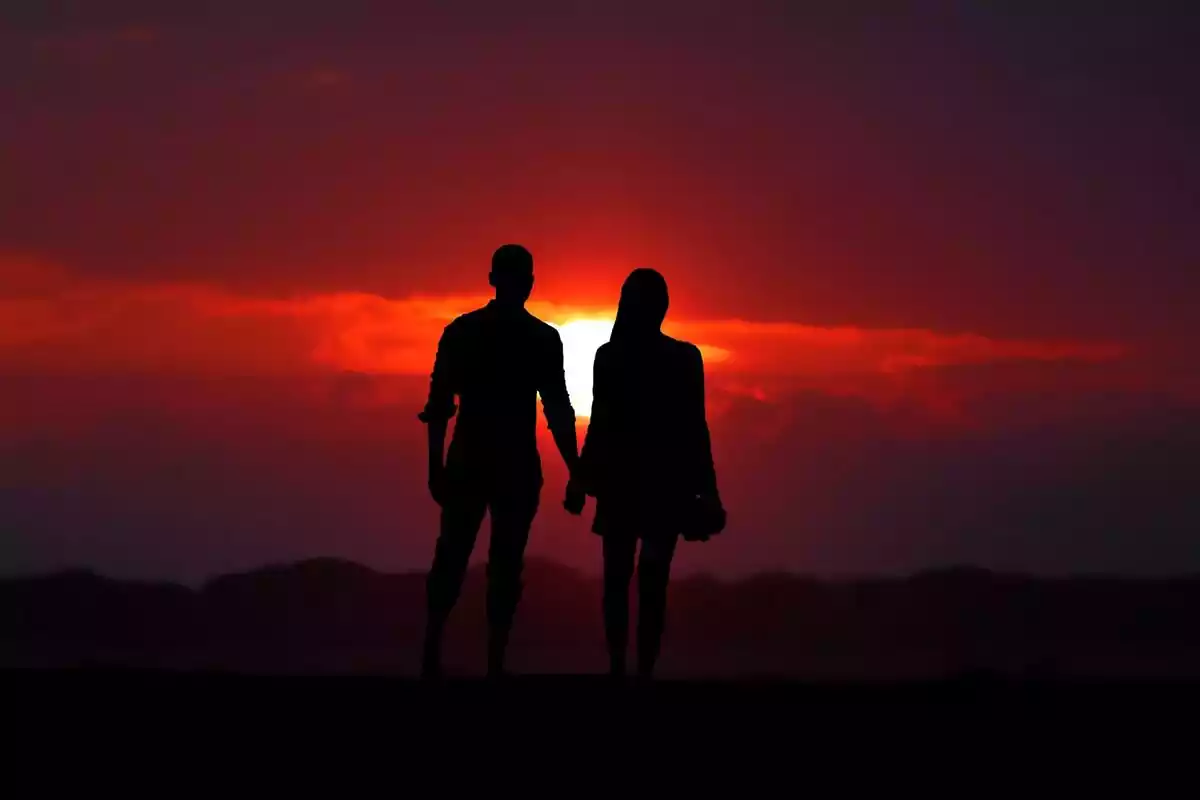 Una pareja de enamorados cogidos de la mano ante la puesta de sol roja