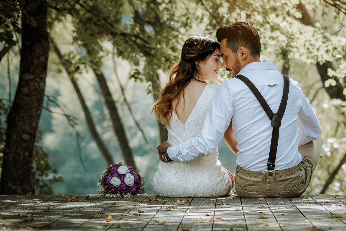 Una pareja recién casada, con la ropa de la boda puesta, besándose bajo un árbol