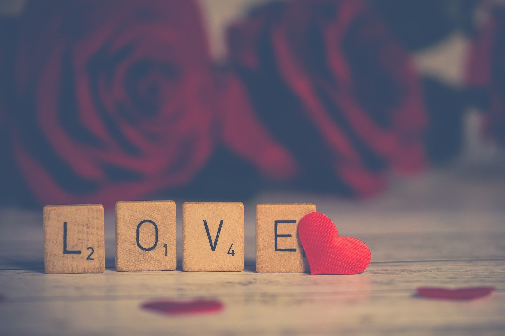 Piezas de madera con la palabra 'love' y un corazón al lado, con unas rosas detrás en segundo plano